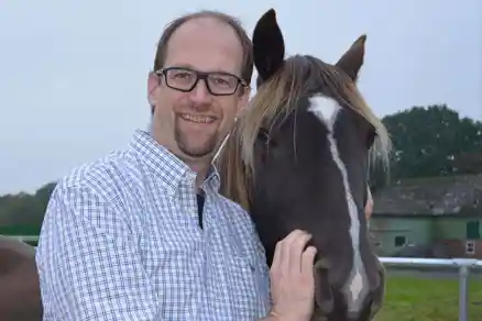 Kontaktpersoner 8 En man håller fast huvudet på en svart häst som står till höger om honom och ler. Man ser bara deras huvuden. I bakgrunden skymtar man en lada och en äng, men det är den ljusa himlen som dominerar bilden.
