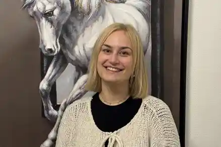 Kontaktpersoner 4 En kvinna ler och tittar rakt in i kameran. Bakom henne hänger en tavla som föreställer ett häst.